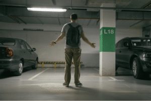A man stands in a parking garage with a green sign that says L18