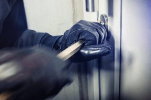 A person wearing black gloves is opening a door with a crowbar