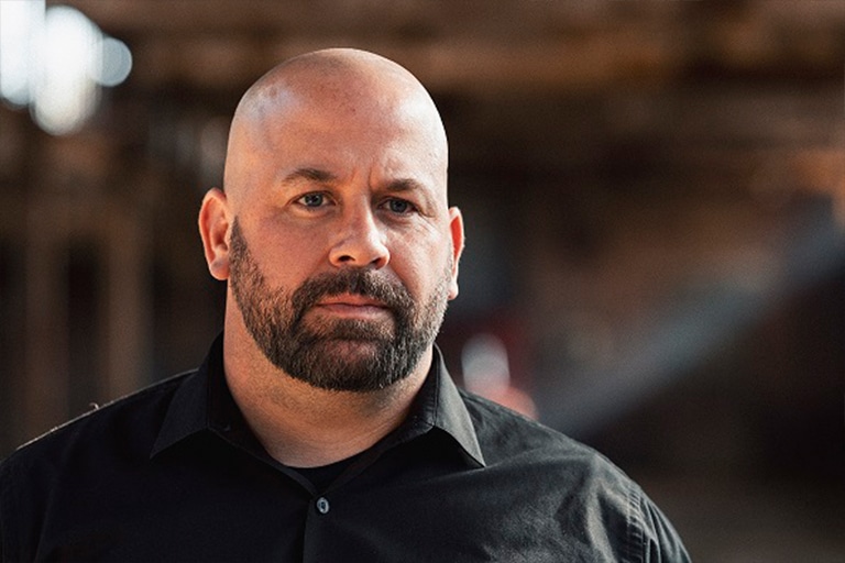 A man with a beard is wearing a black shirt and looking at the camera