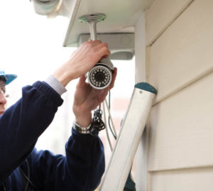 A man is installing a security camera on the side of a building