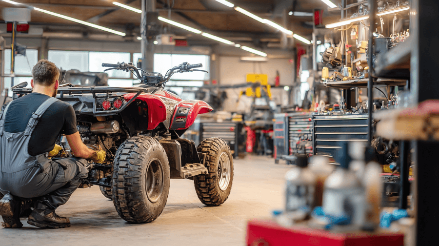 A mechanic works on a red ATV inside a well-equipped repair shop, surrounded by tools, parts, and organized workbenches.